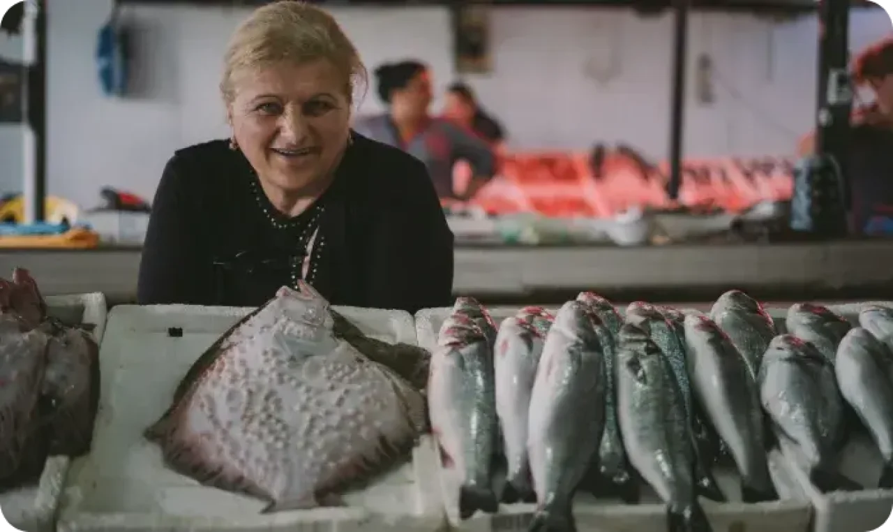 A cheerful woman looks at the camera while displaying all the fishes she is selling.