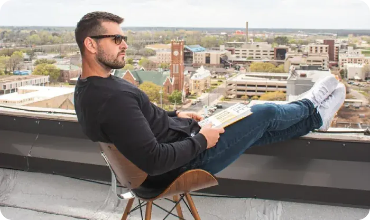 Man with sunglasses and book sitting on balcony
