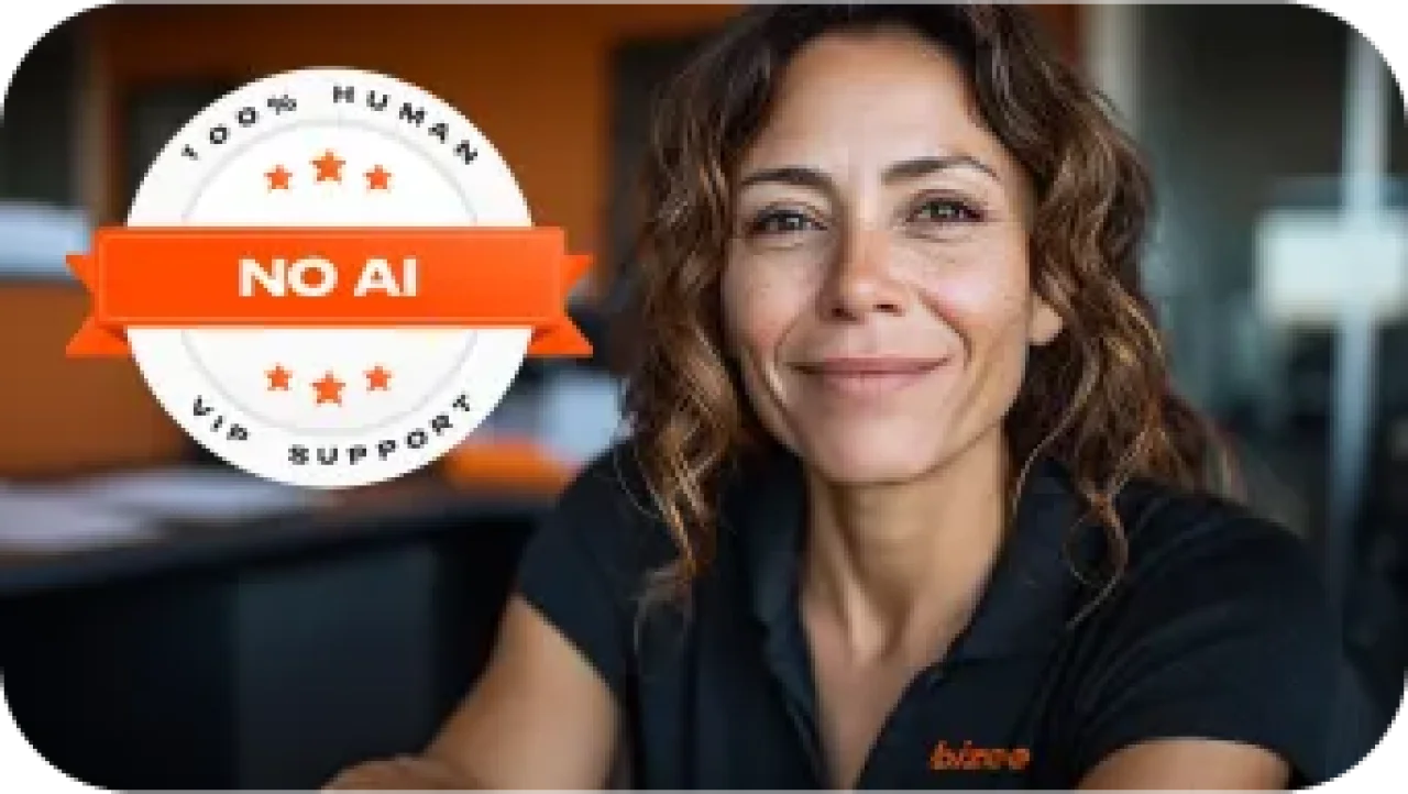 Bizee customer support agent smiling in office, wearing a black Bizee shirt, with a “100% Human, No AI, VIP Support” badge in the corner.