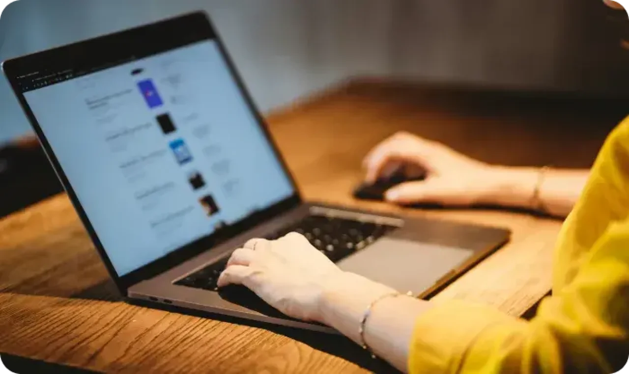 Person browsing website on laptop at wooden desk