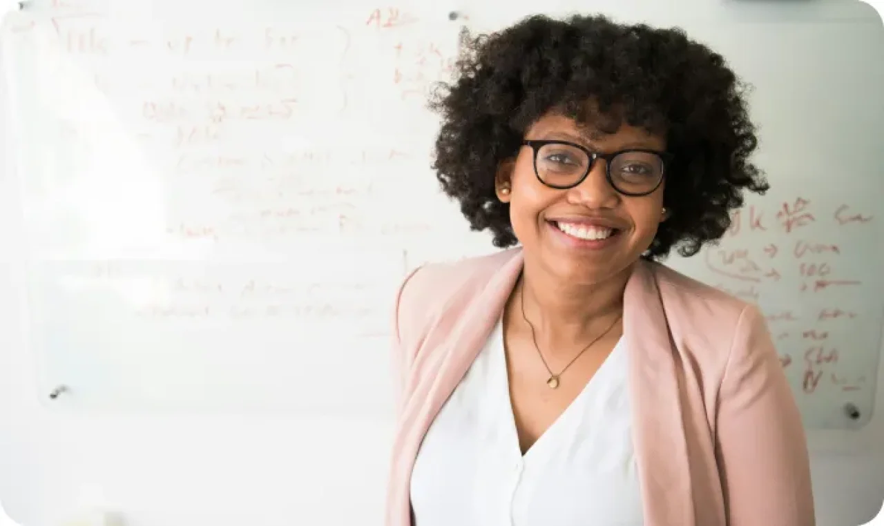 Confident businesswoman smiling in front of a whiteboard during a meeting or presentation in an office setting.