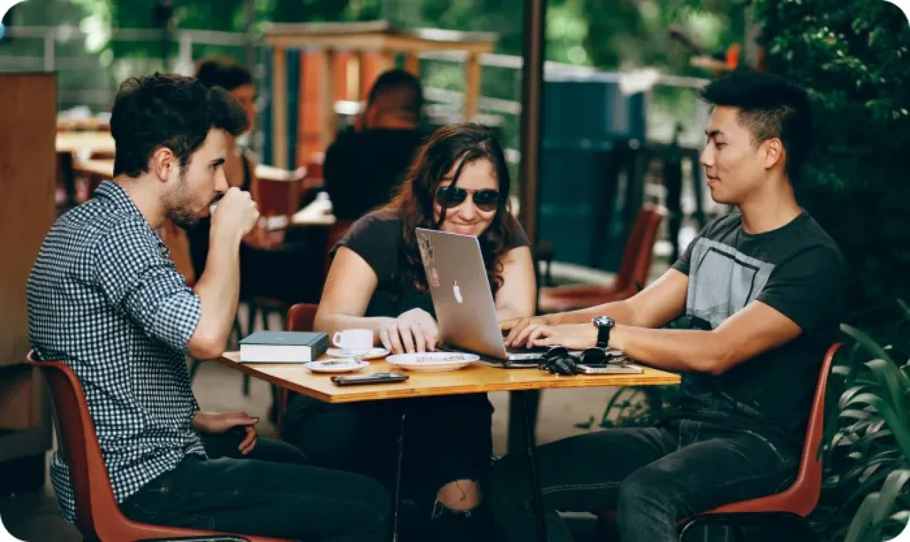 Three young professionals collaborating outdoors at a cafe, working together on a laptop.