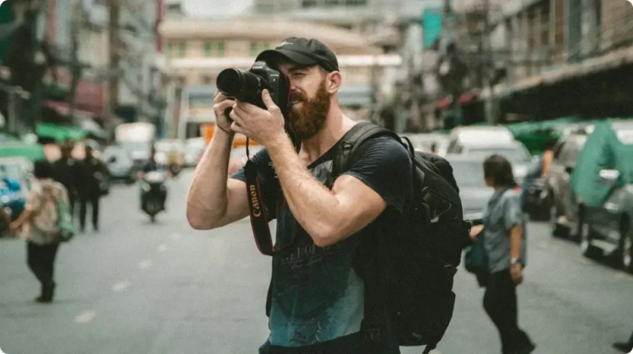 Male travel photographer taking street photos in busy urban city with Canon DSLR camera and backpack